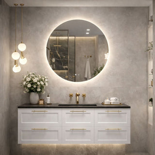 Šviesus vonios kambarys su pakabinama spintele, juodu stalviršiu, auksiniais maišytuvais ir apvaliu veidrodžiu su švelniu LED apšvietimu.