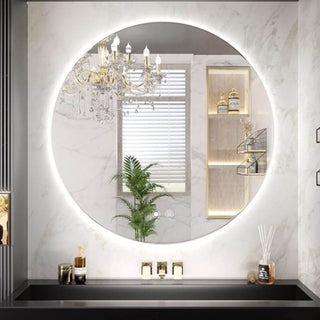 Modernus apvalus veidrodis vonios kambaryje su tolygiai paskirstyta LED juosta aplink krasta, marmurine siena ir juodu stalvirsiu.