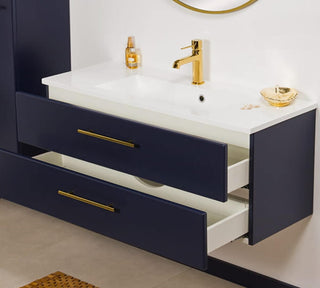 Stilinga pakabinama tamsiai mėlyna vonios spintelė su dviem talpiais atveriamais stalčiais ir auksinėmis rankenėlėmis, papildyta moderniu praustuvu.