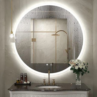 Apskritas LED veidrodis su šviesos rėmu virš marmurinio stalviršio ir gėlių puokšte vonios kambaryje.