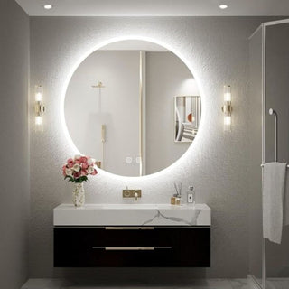 Apšviestas apskritas veidrodis virš minimalistinio praustuvo su rožių puokšte ir stiklinėmis sieninėmis lempomis.